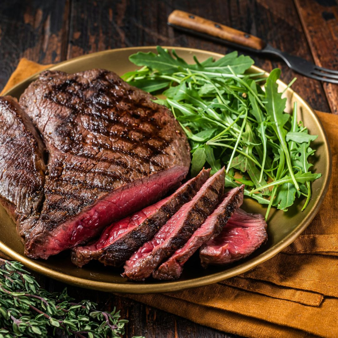 BBQ dinner with top sirloin beef steak and salad on a plate. Wooden background. Top view