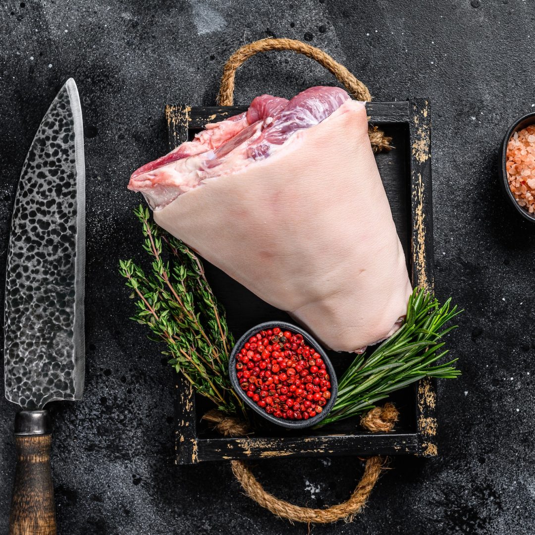 Fresh Raw pork Eisbein knuckle ham in a wooden tray with meat knife.